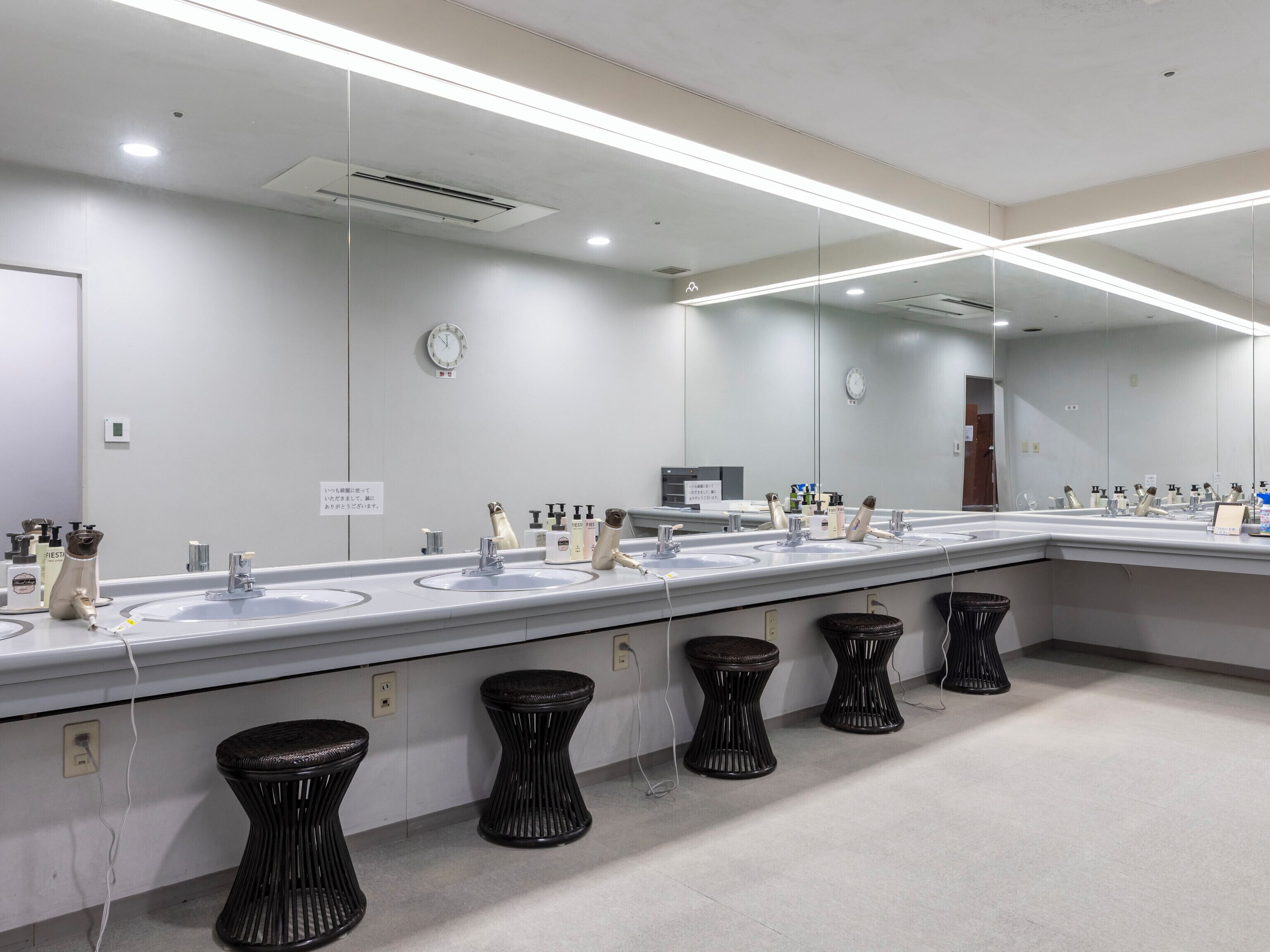 A modern restroom with multiple sinks, black stools, and a large mirror.