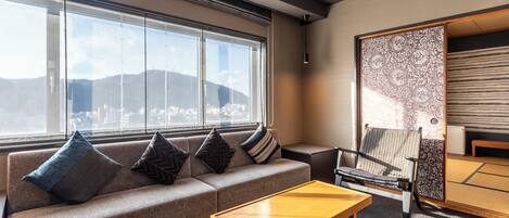 Uma sala de estar moderna com sofá, mesa de centro e vista para um horizonte urbano através de grandes janelas.