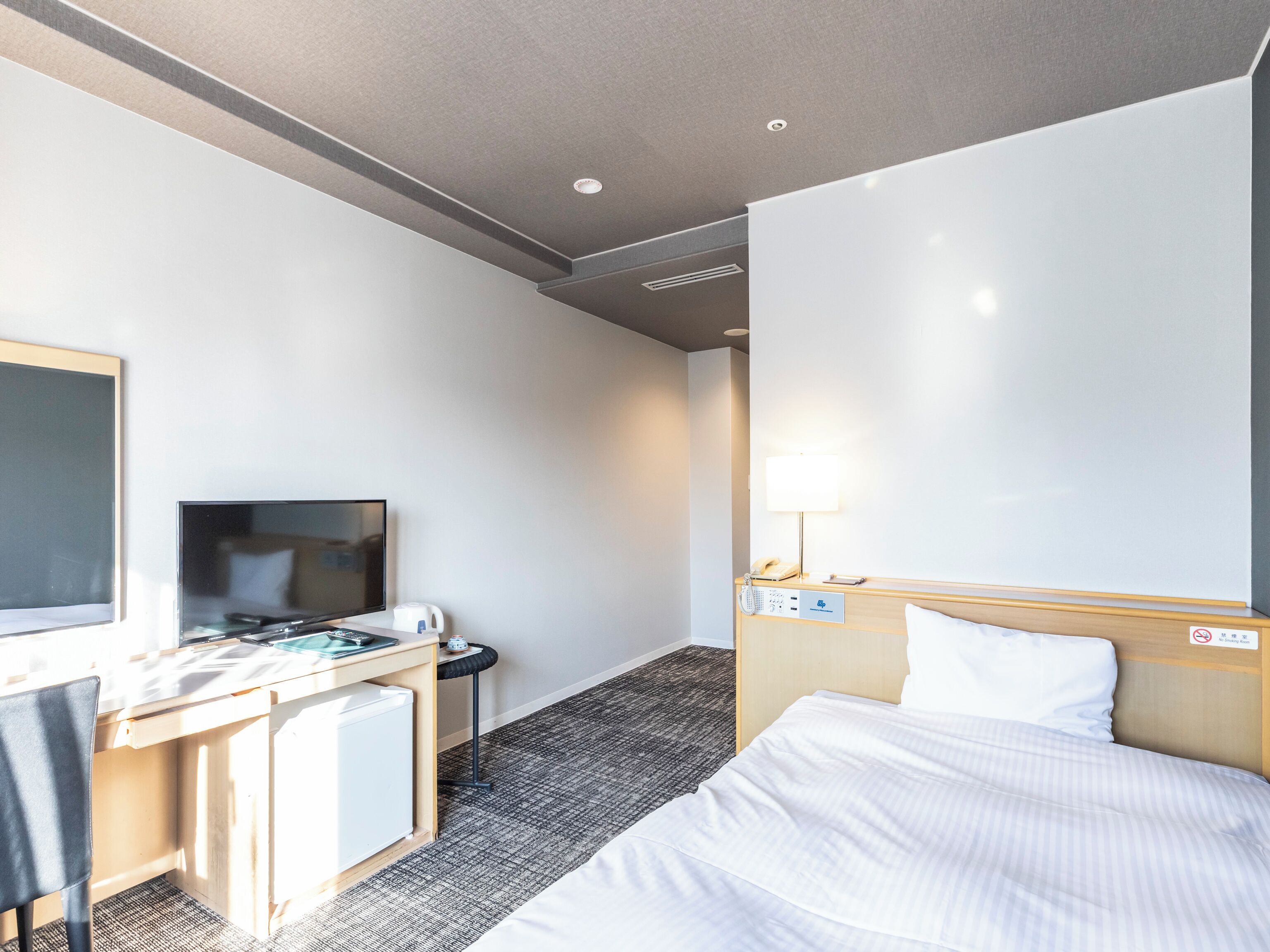 Habitación de hotel con cama, escritorio, computadora, televisor y lámpara.