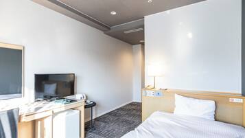 Habitación de hotel con cama, escritorio, computadora, televisor y lámpara.
