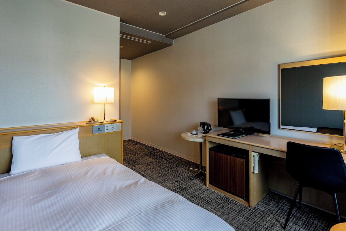 Ett hotellrum med en säng, ett skrivbord, en stol och en tv.