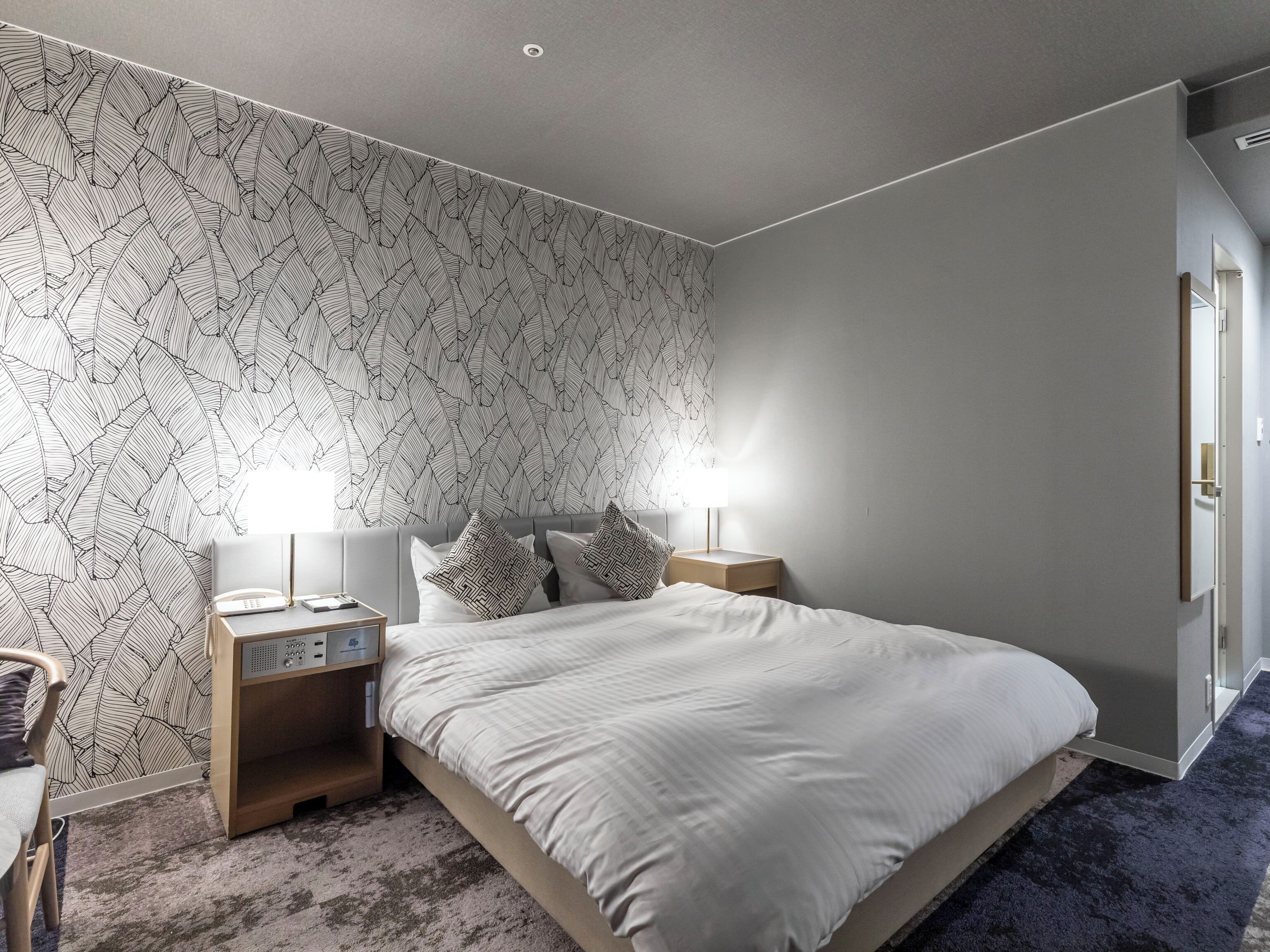 Un dormitorio con una cama grande, dos mesitas de noche con lámparas, una mesita auxiliar y un papel tapiz estampado.