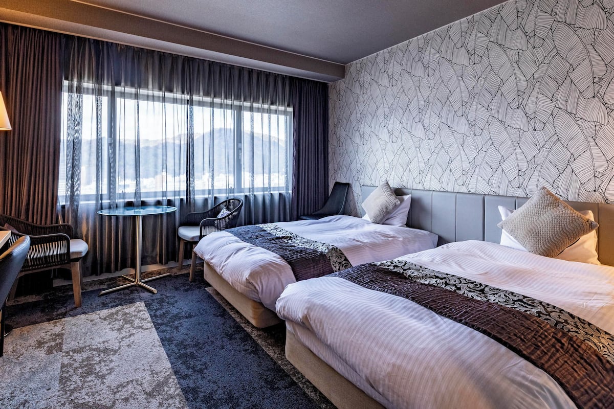 Ett modernt hotellrum med två sängar, ett litet skrivbord och en stol.