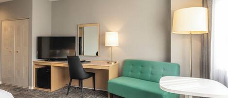 A hotel room with a bed, a desk with a computer, a green sofa, a lamp, and a TV.