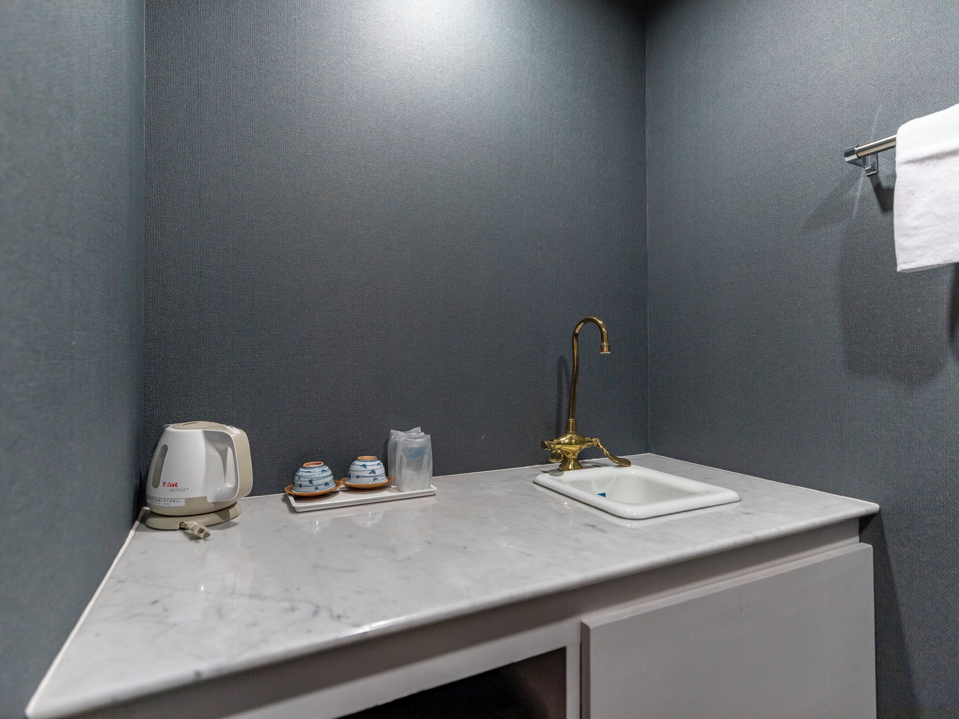 A bathroom with a white sink, a gold faucet, and a towel hanging on the wall.