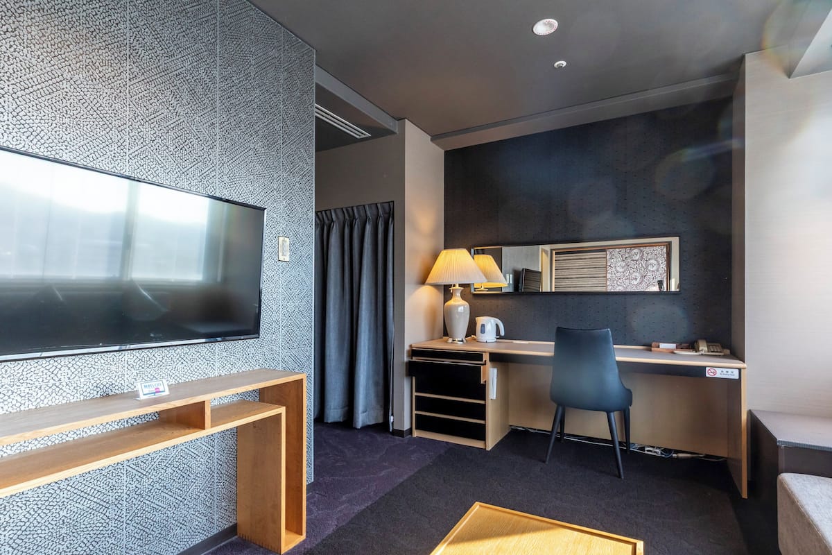 Ett modernt hotellrum med en platt-TV, ett skrivbord med en lampa, en stol och ett litet soffbord.