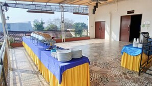 Un espace extérieur abrité, aménagé pour les repas, avec une longue table dressée, des assiettes et une nappe bleue.