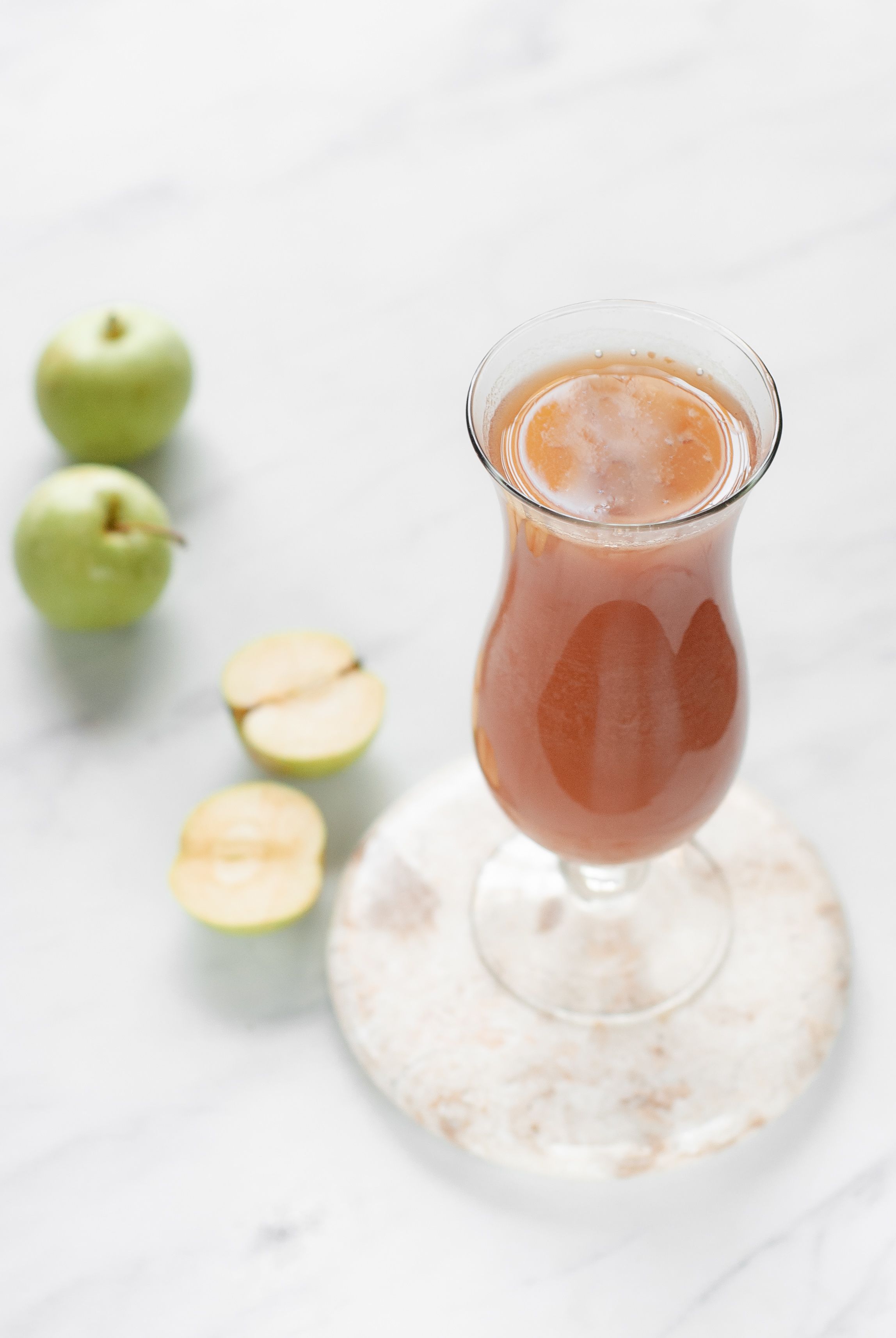 Un vaso de bebida rosada con rodajas de manzana sobre un posavasos de mármol.