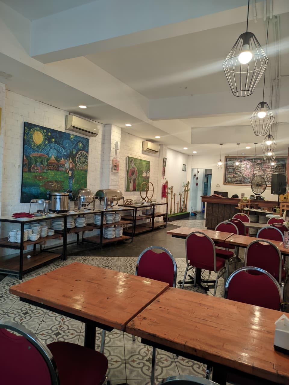 Een restaurant met houten tafels en rode stoelen, een muurschildering en hangende pendantlampen.