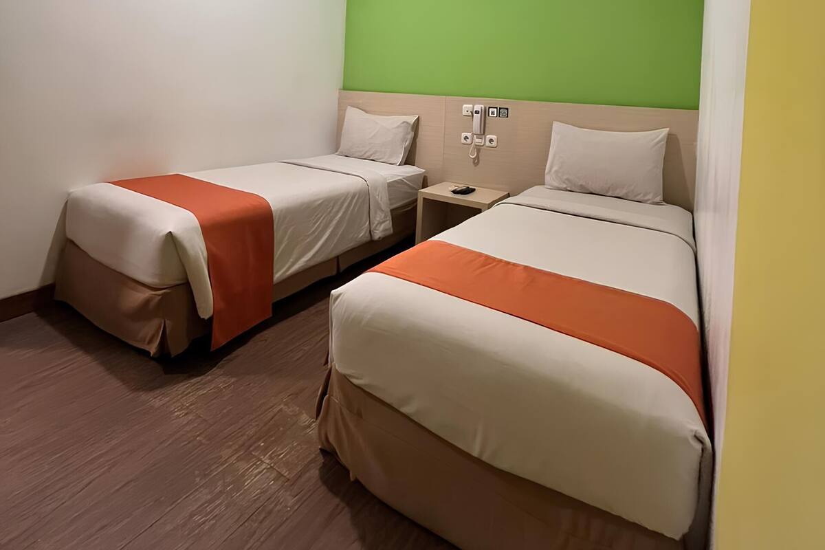 Une chambre d’hôtel avec deux lits simples, un mur d’accent de couleur verte et un plancher en bois.
