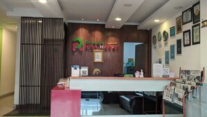 Un espace d’accueil d’hôtel avec un comptoir en bois, un présentoir rouge et un mur orné de certificats encadrés.