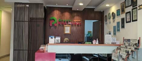 A hotel reception area with a wooden reception desk, a red counter, and a wall with framed certificates.