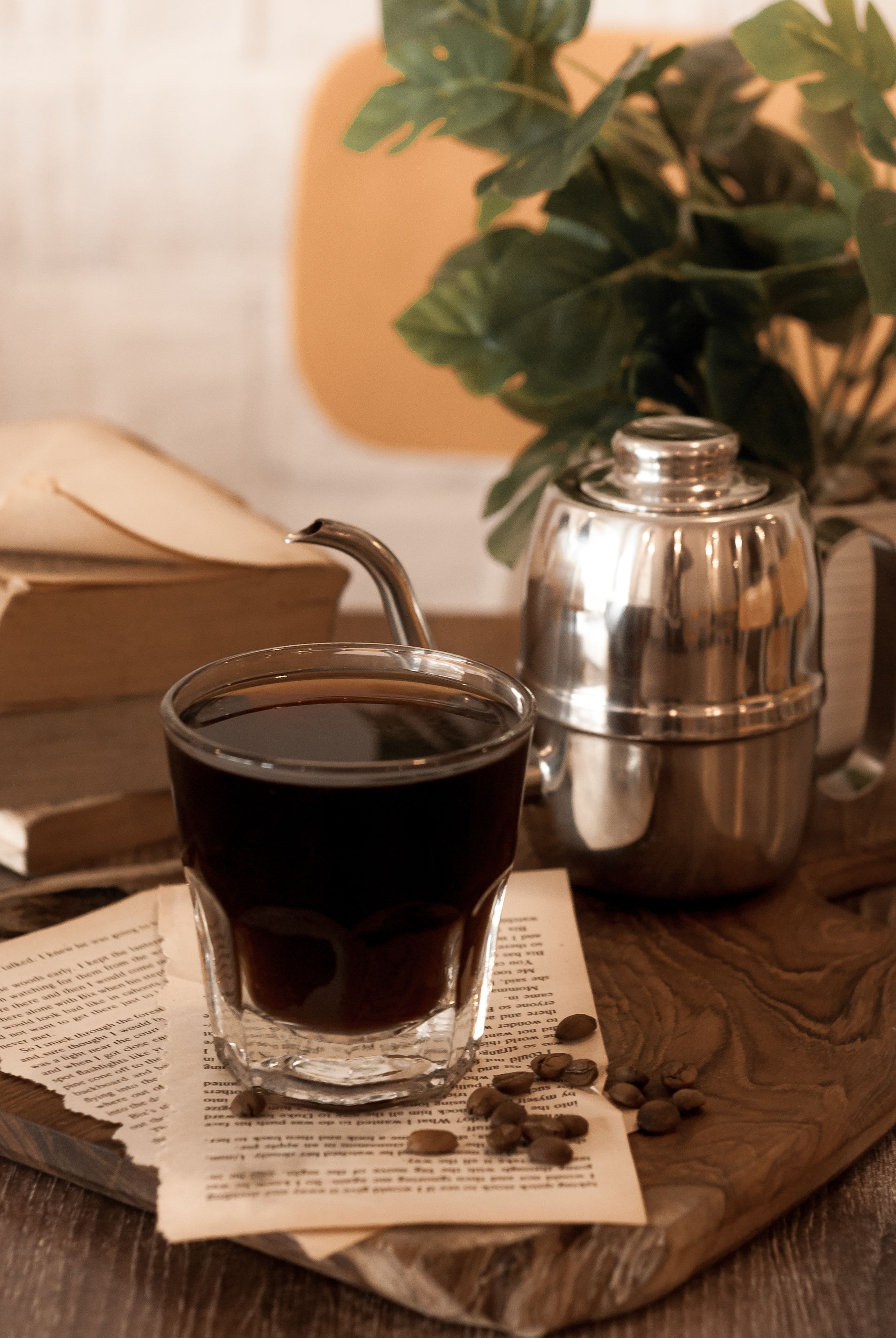 Un verre contenant un liquide sombre, peut-être du café, posé sur une surface en bois, avec un récipient en métal et des livres en arrière-plan.