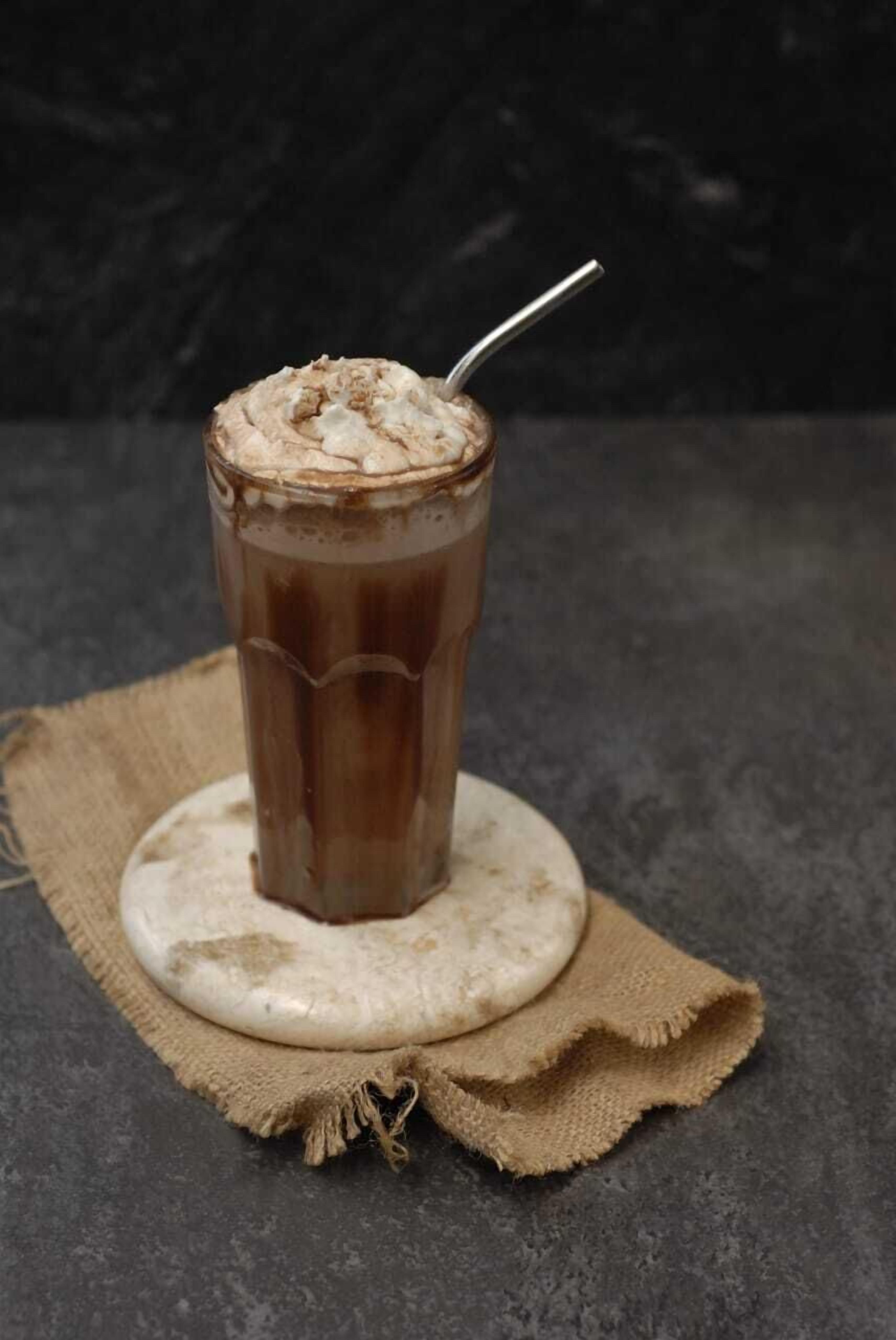 Um copo alto de chocolate com chantilly sobre um apoio de palha.