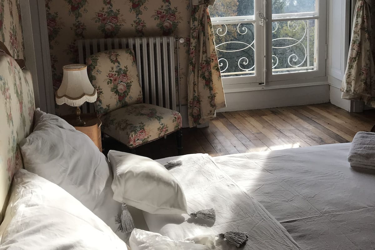 Un dormitorio con cama, una silla, un radiador y una ventana con cortinas.