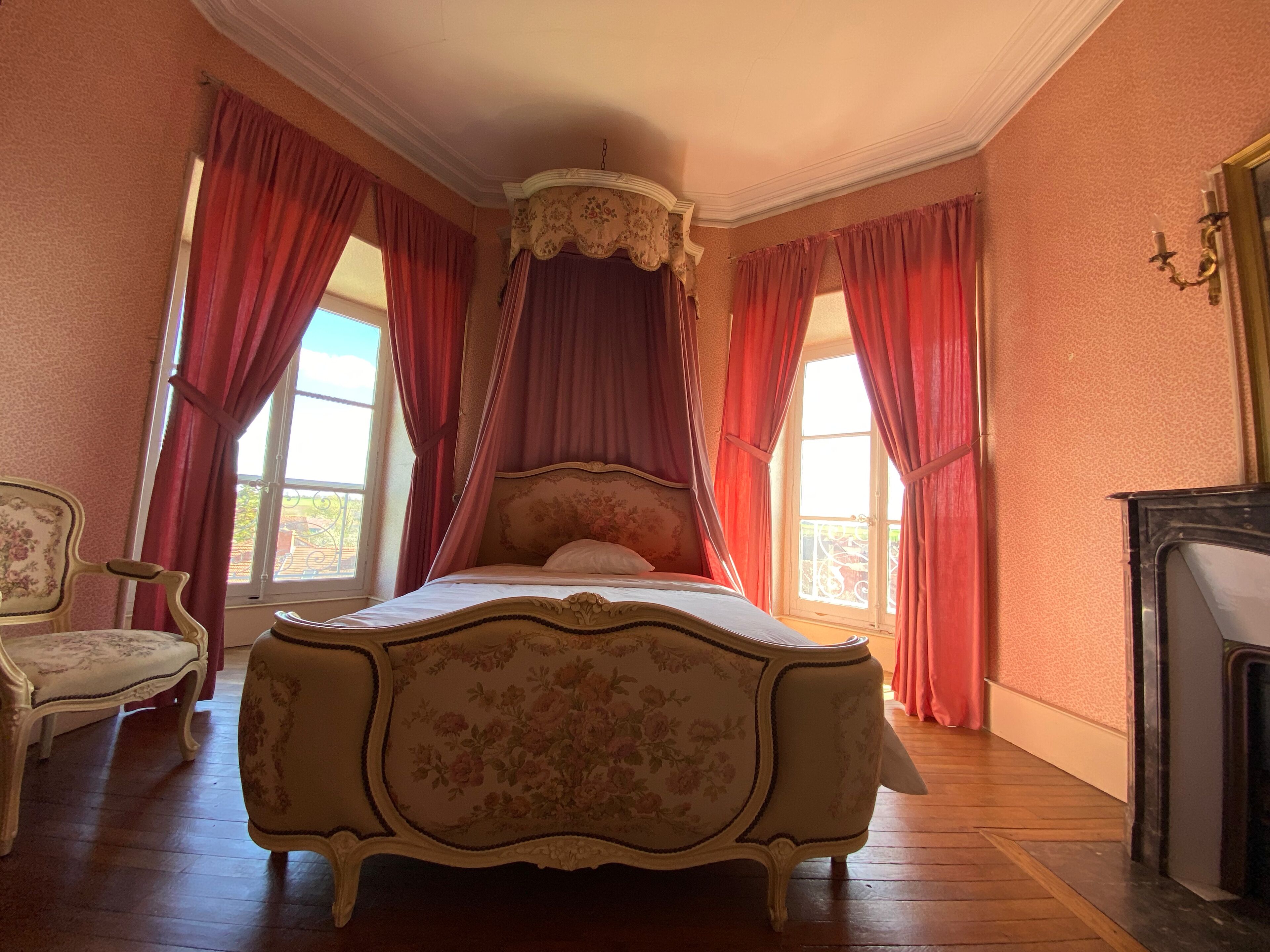 A bedroom with a four-poster bed, a chair, and a fireplace.