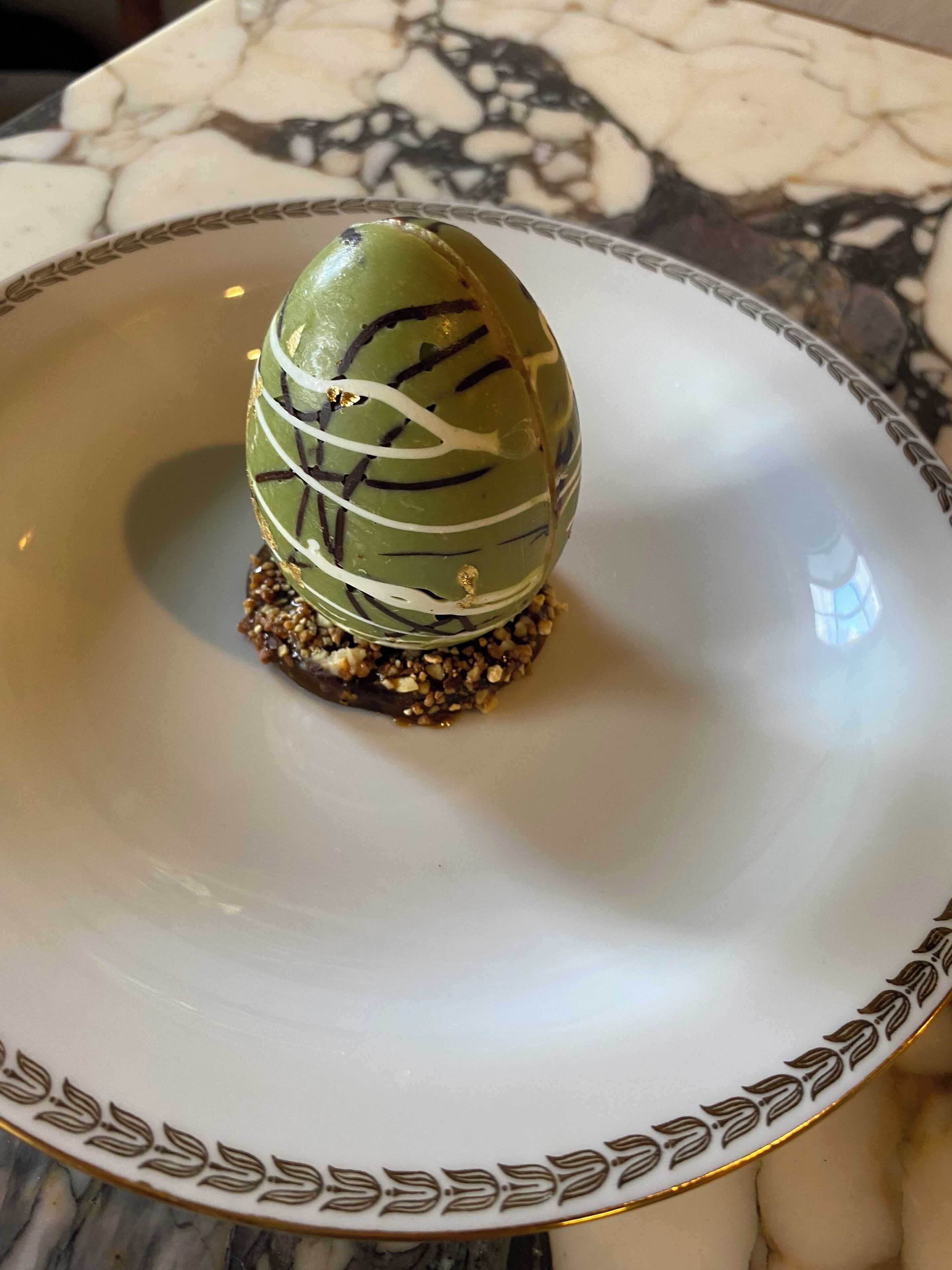 Un postre sobre un plato blanco con borde dorado, colocado sobre una mesa de mármol.