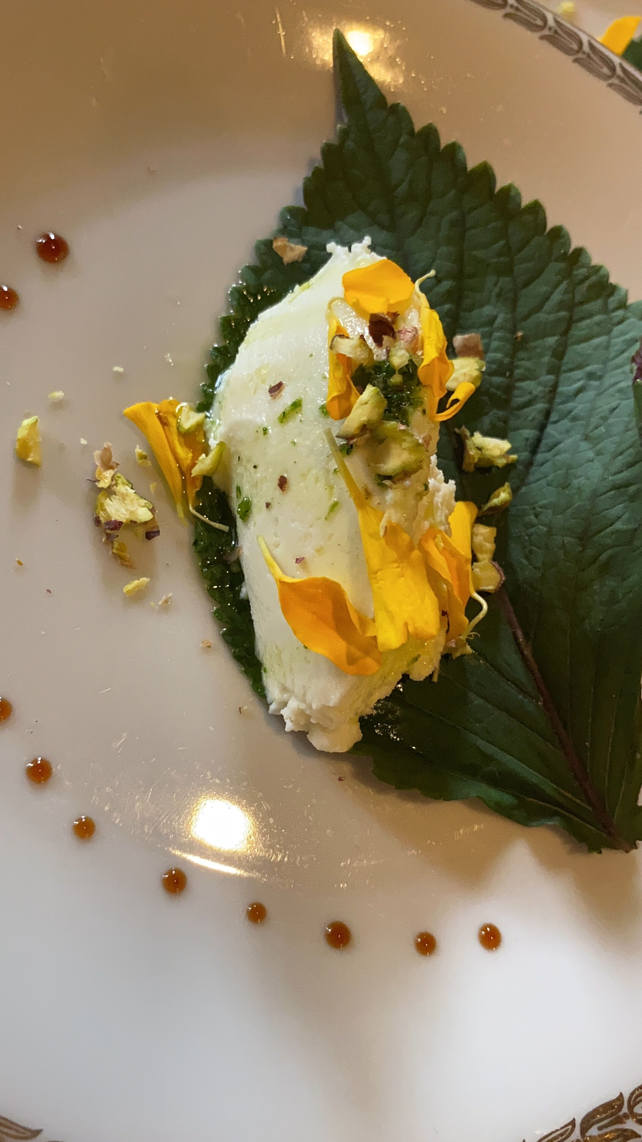 Un postre en un plato con una hoja decorativa y almíbar esparcido.
