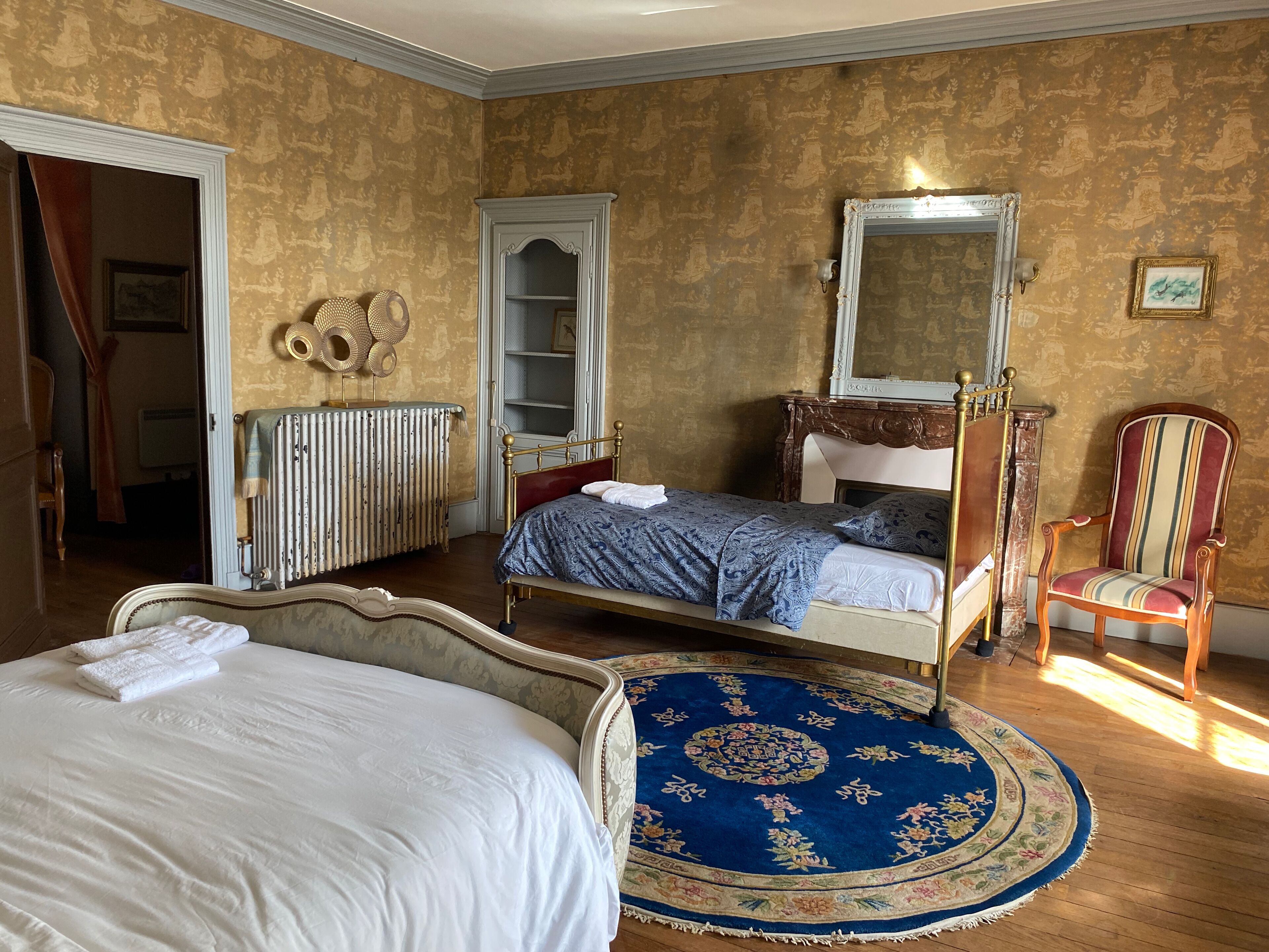A bedroom with a four-poster bed, a large mirror, a wooden chair, and a radiator.