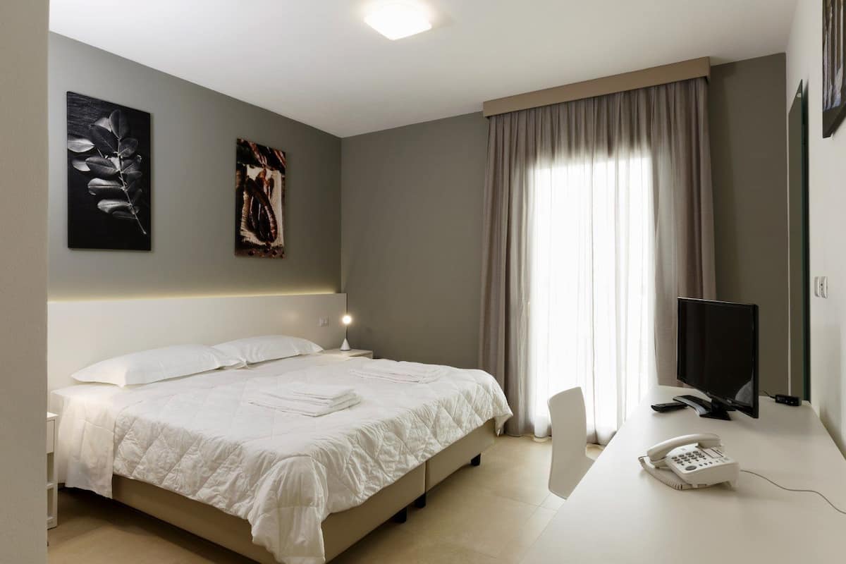 Una habitación de hotel con una cama, un escritorio con teléfono, un televisor y obras de arte en las paredes.