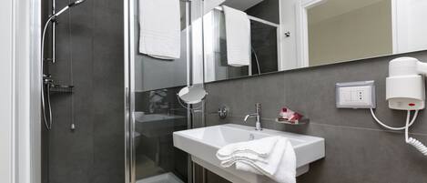 A modern bathroom with a glass-enclosed shower, a white sink, a mirror, and a hairdryer on the wall.