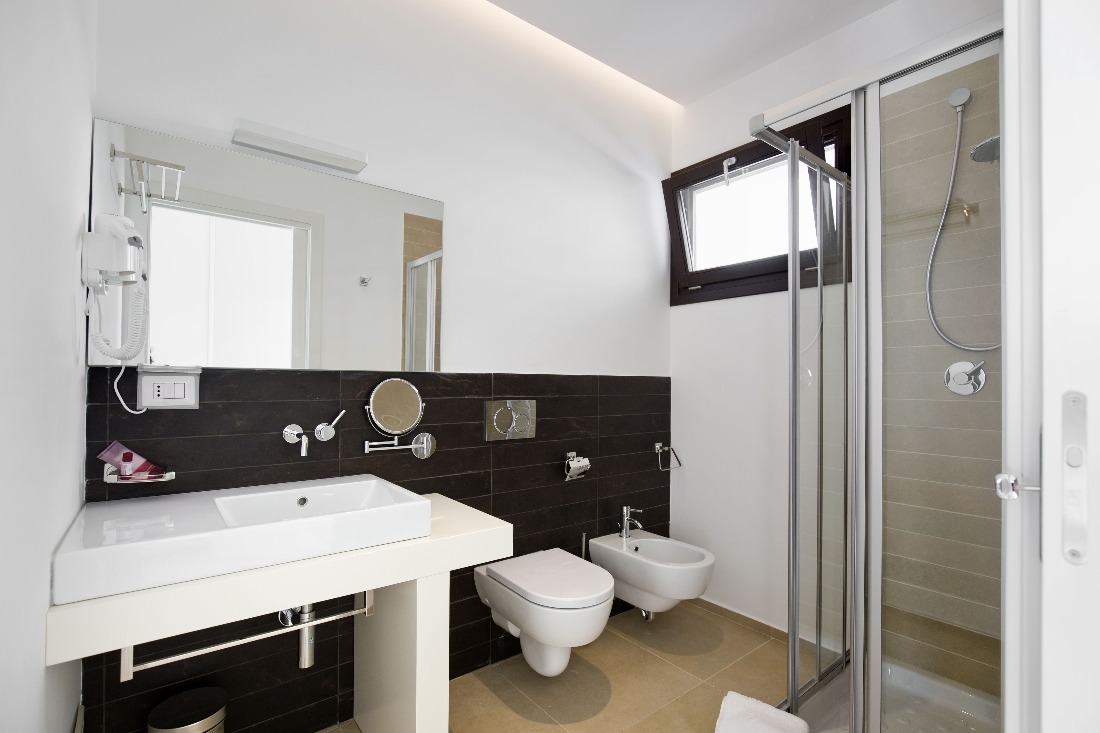 Ein modernes Badezimmer mit einem weißen Waschbecken, einer Toilette, einem Bidet und einer Duschkabine aus Glas.