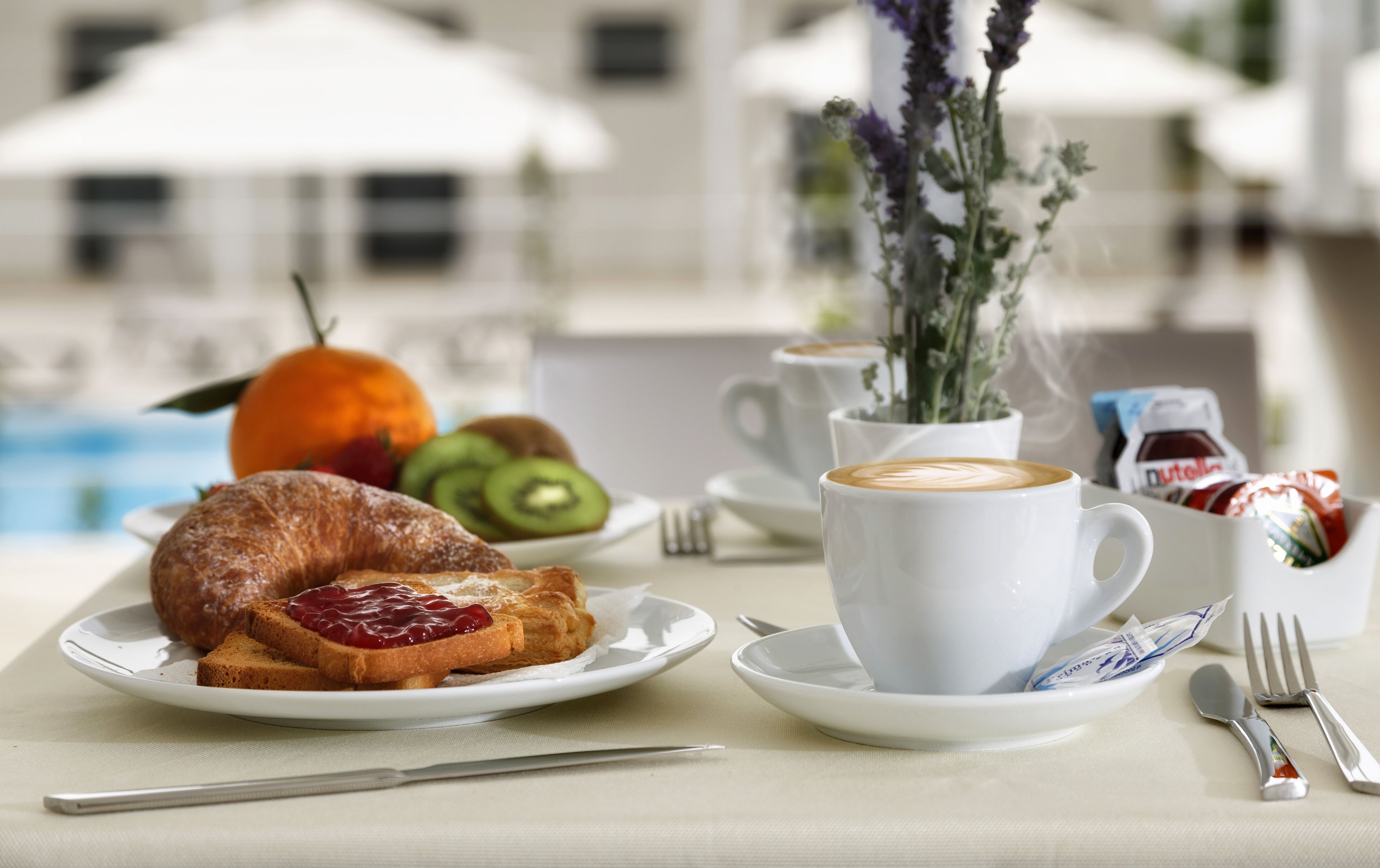 Mesa posta para o café da manhã, com croissants, frutas, café e acompanhamentos.
