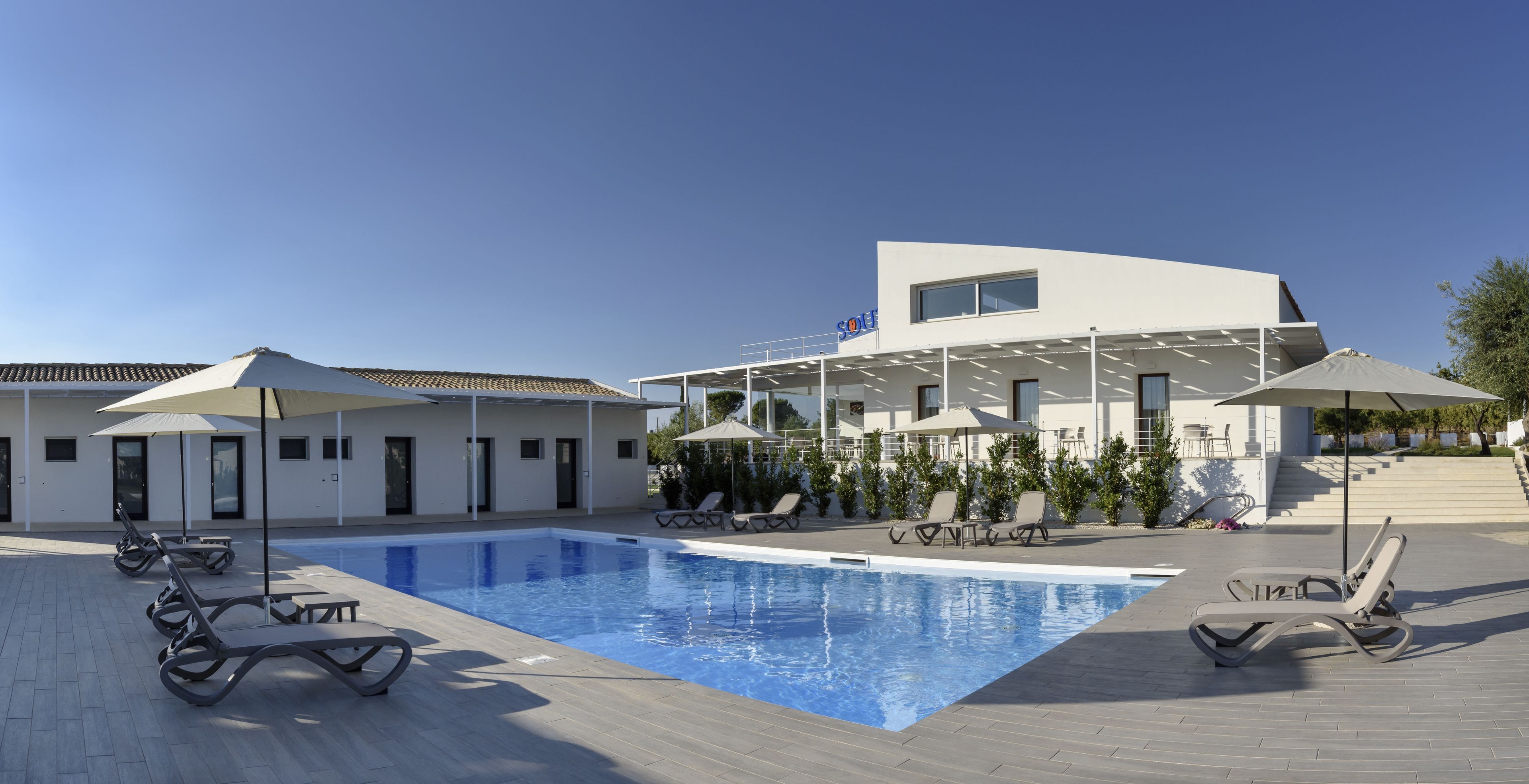 Ein modernes Hotel mit Schwimmbad, Liegestühlen und Sonnenschirmen.