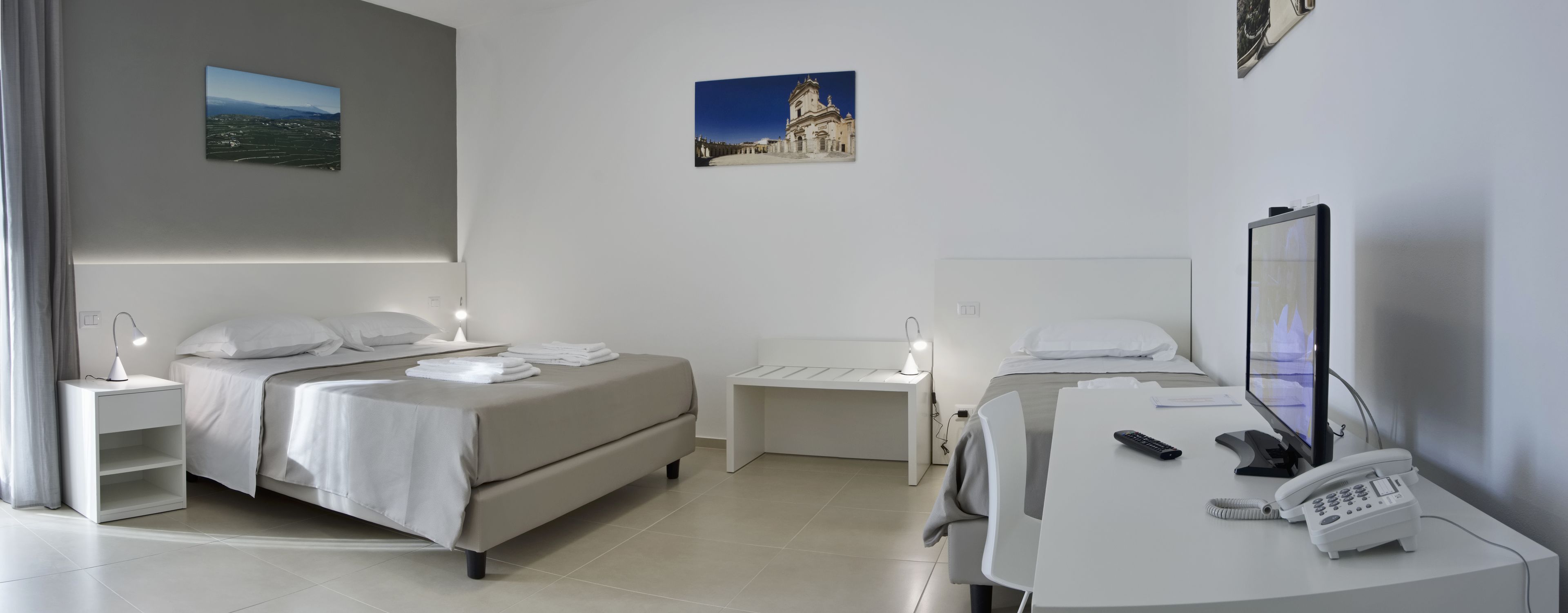 A hotel room with two beds, a desk with a phone, and artwork on the walls.