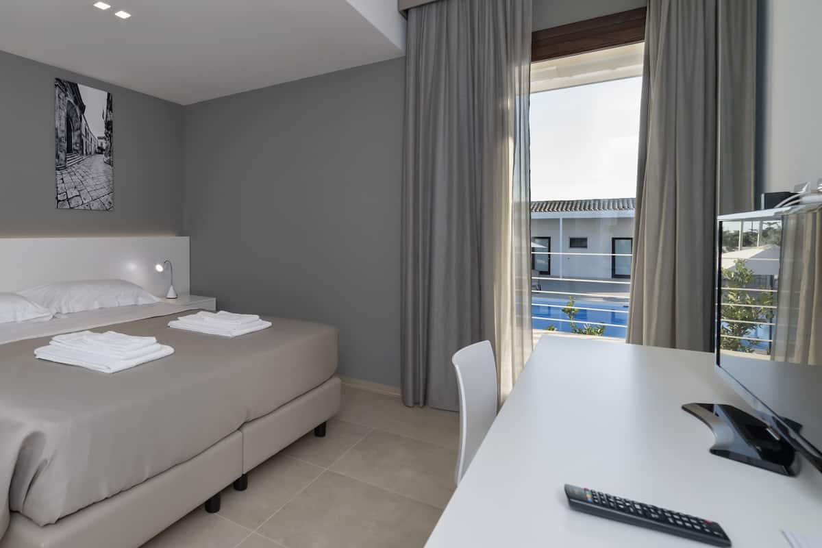 Una habitación de hotel moderna con cama, escritorio, silla, control remoto y ventana con cortinas.