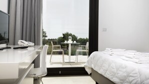 Una habitación de hotel moderna con una cama, un escritorio con teléfono y una mesa con sillas frente a un ventanal grande.