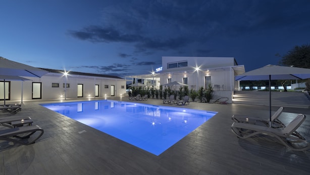 Un hotel moderno con piscina, sillas de descanso y sombrillas.