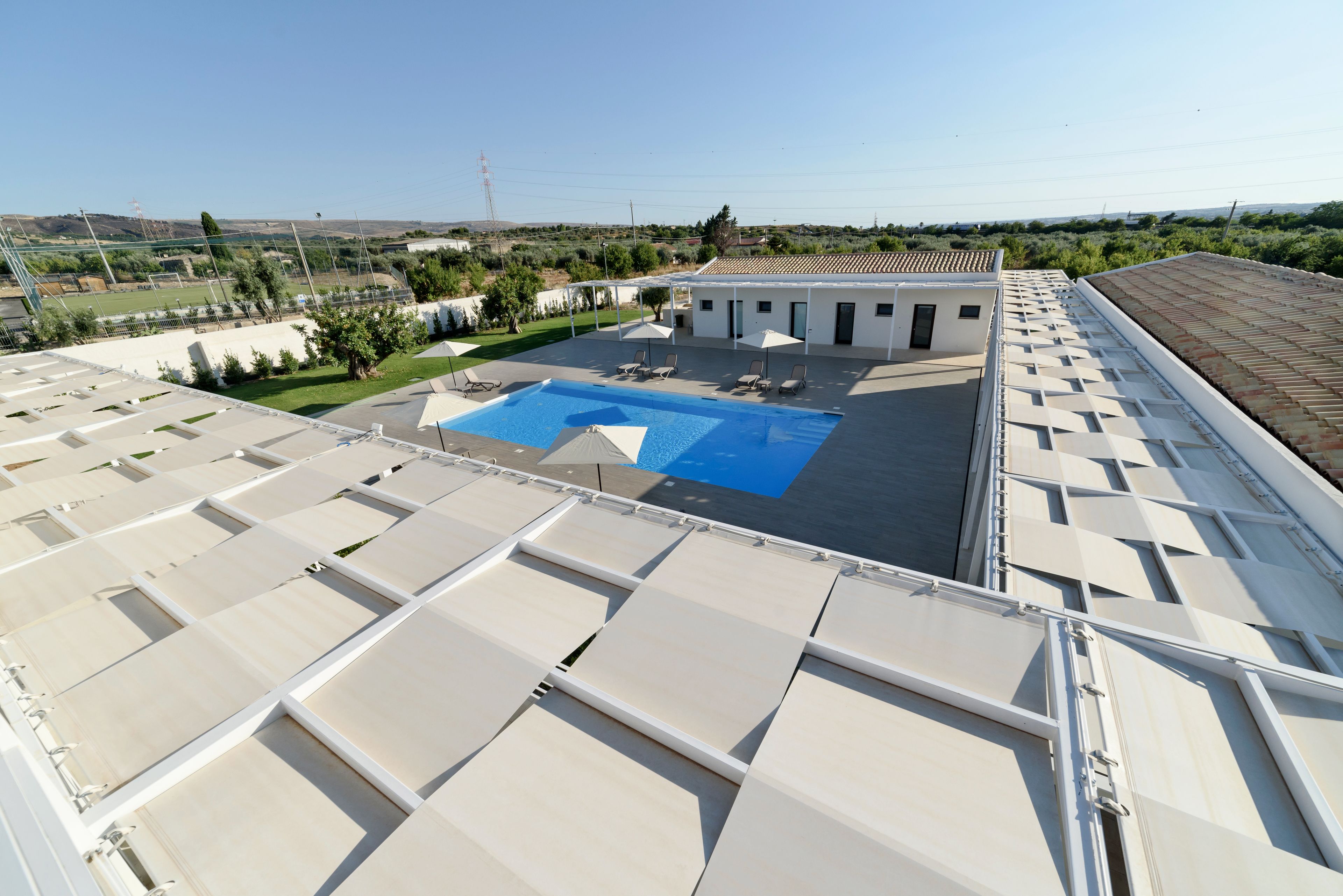 A rooftop with a swimming pool, sun loungers, and a view of the surrounding landscape.