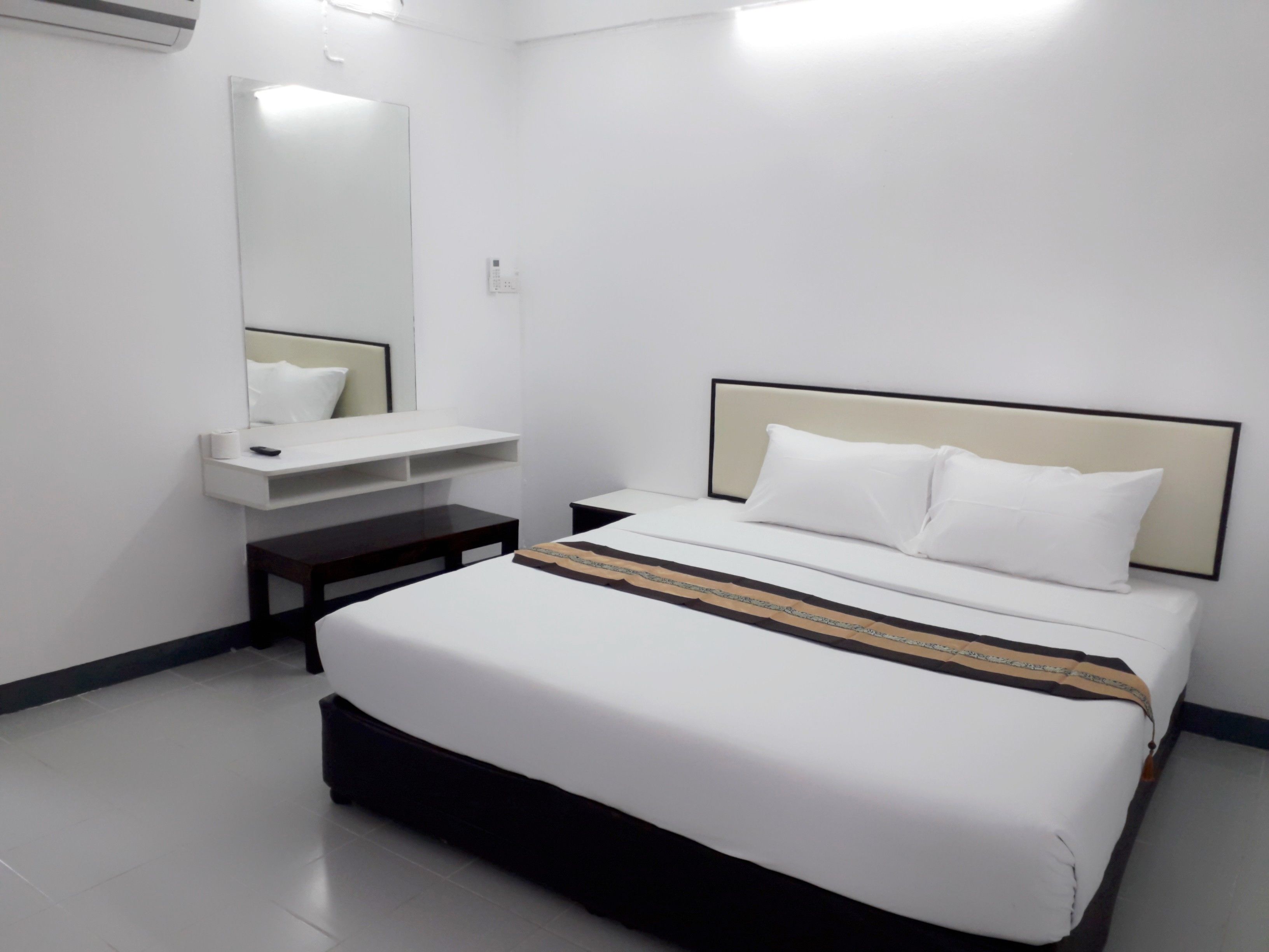 Une chambre d’hôtel avec un grand lit, une table de chevet, un miroir et une petite étagère.