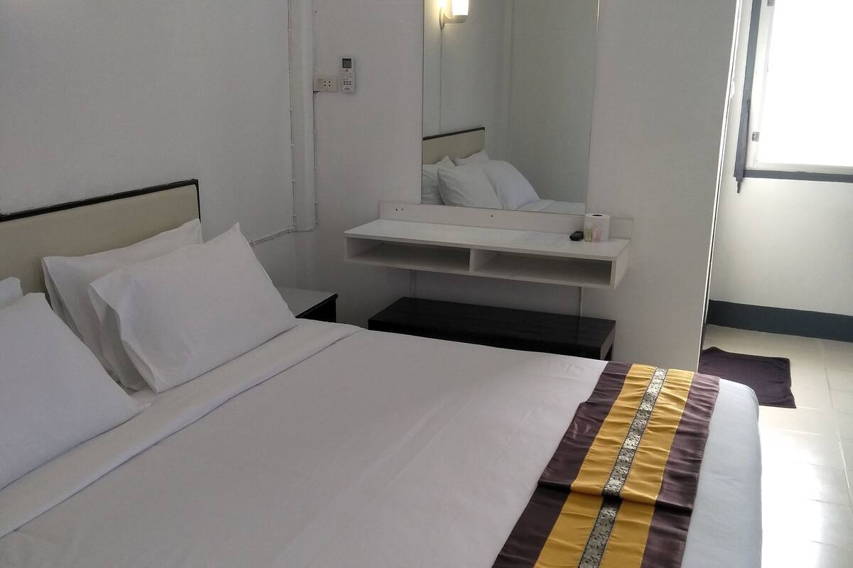 Quarto de hotel com uma cama grande, mesa de cabeceira, espelho e janela.