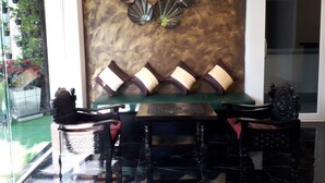 Un coin repas avec une table et des chaises vertes, un mur décoratif orné d’un motif de feuilles et une plante en pot sur la gauche.