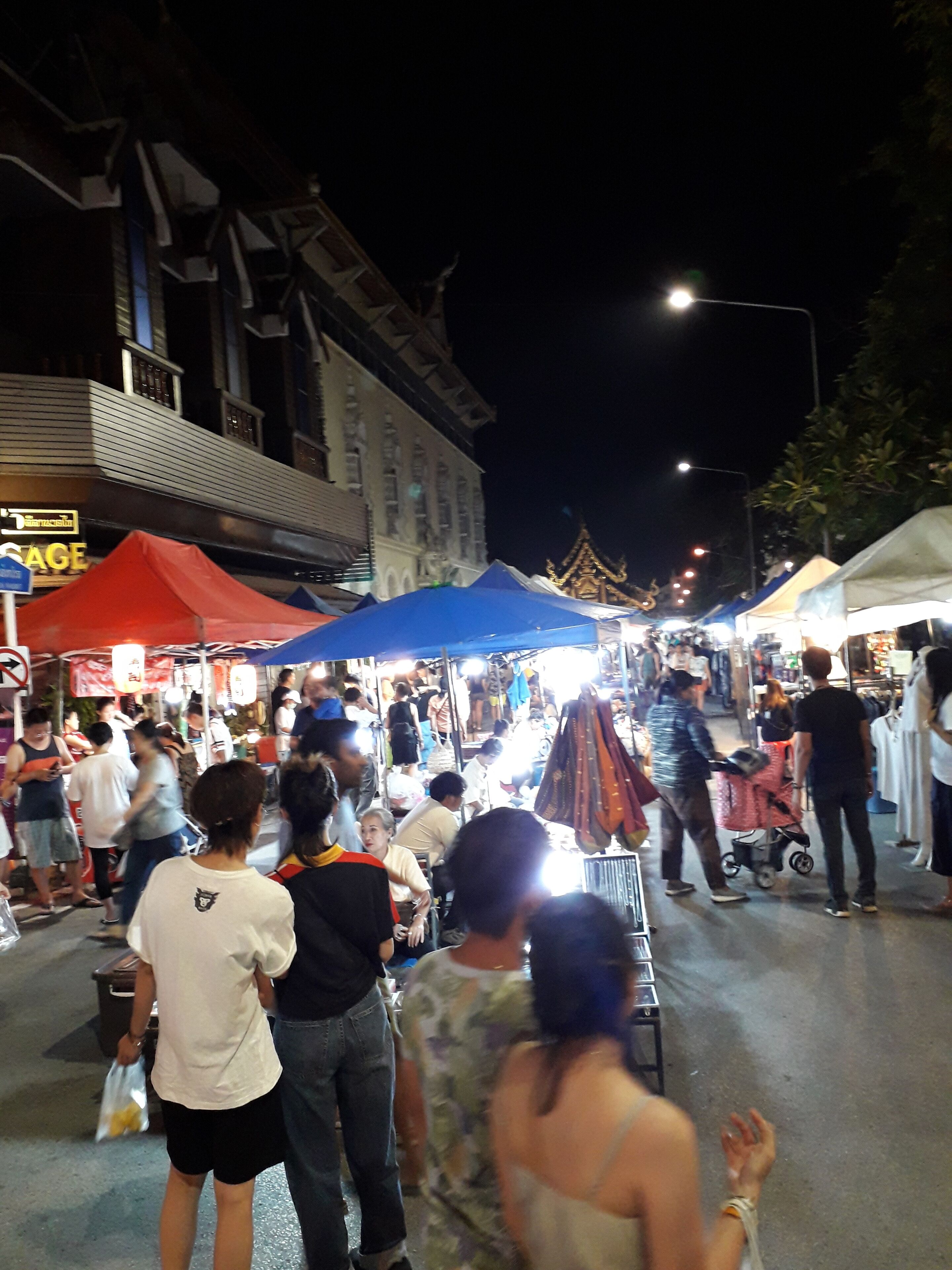 A crowded street market with people shopping and vendors selling goods.