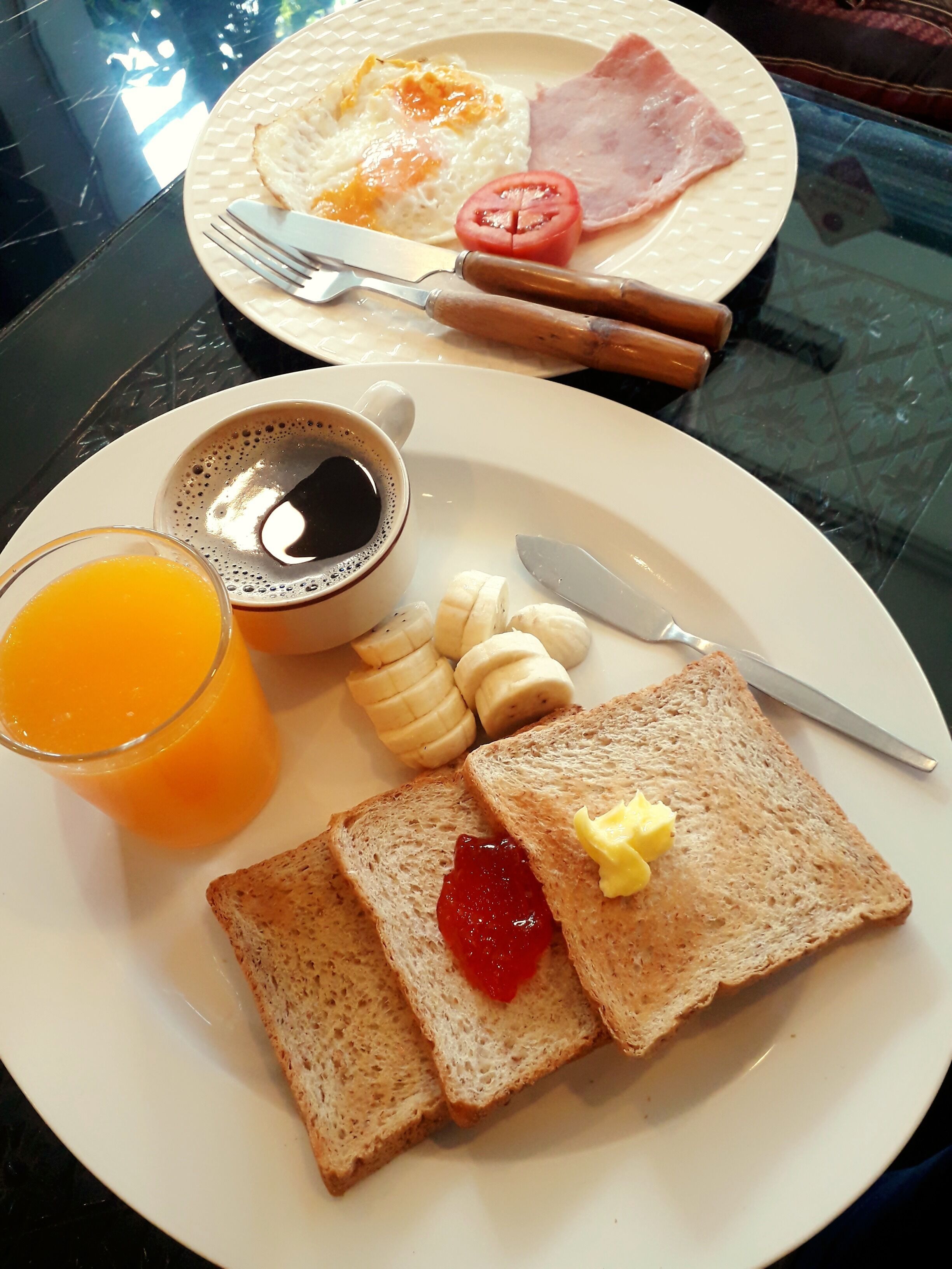 Une assiette de petit-déjeuner avec des toasts, de la confiture, du beurre, une banane, une tomate et une tasse de café.