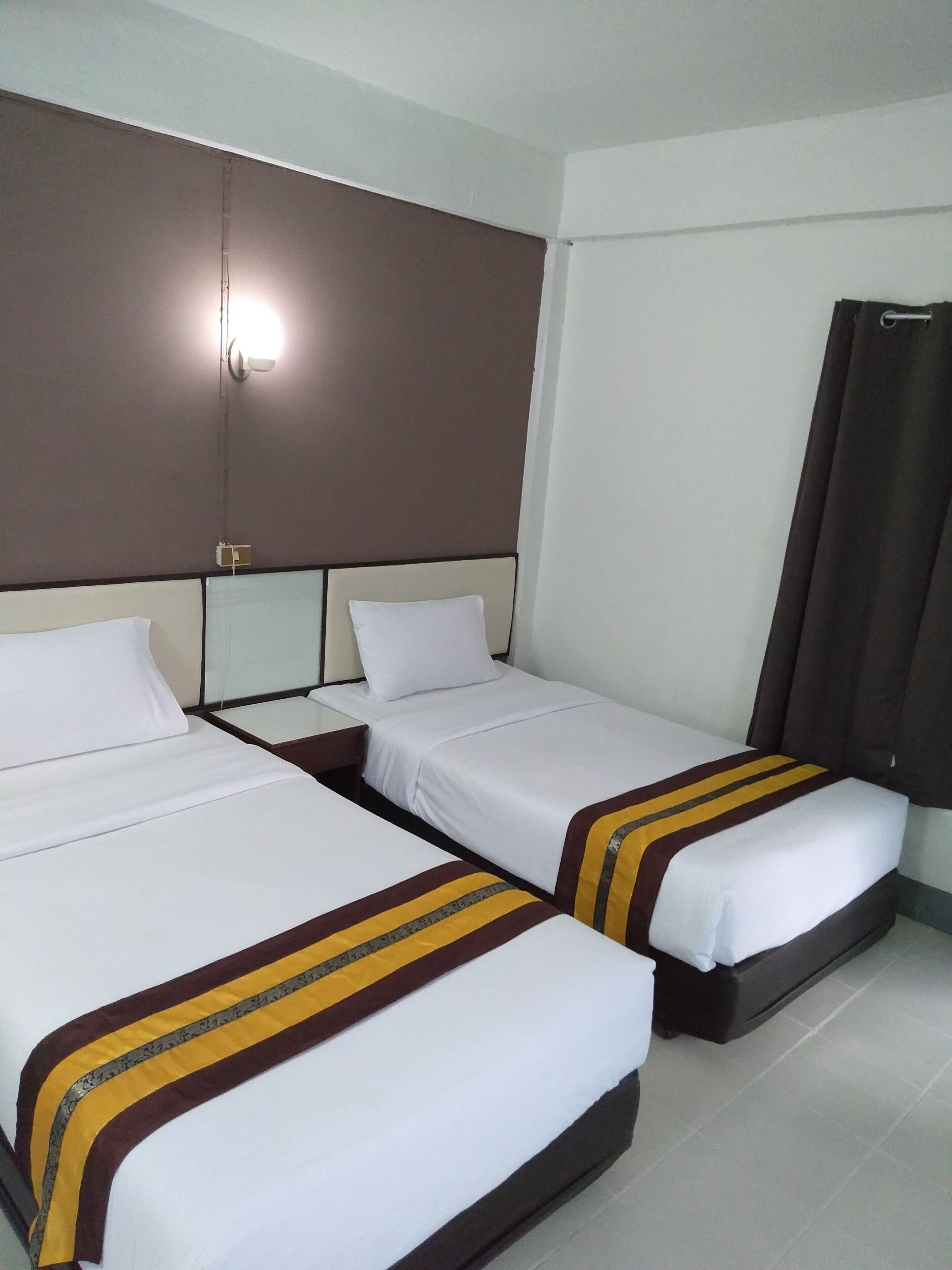 Habitación de hotel con dos camas individuales, un televisor de pantalla plana grande y una cortina oscura en la ventana.