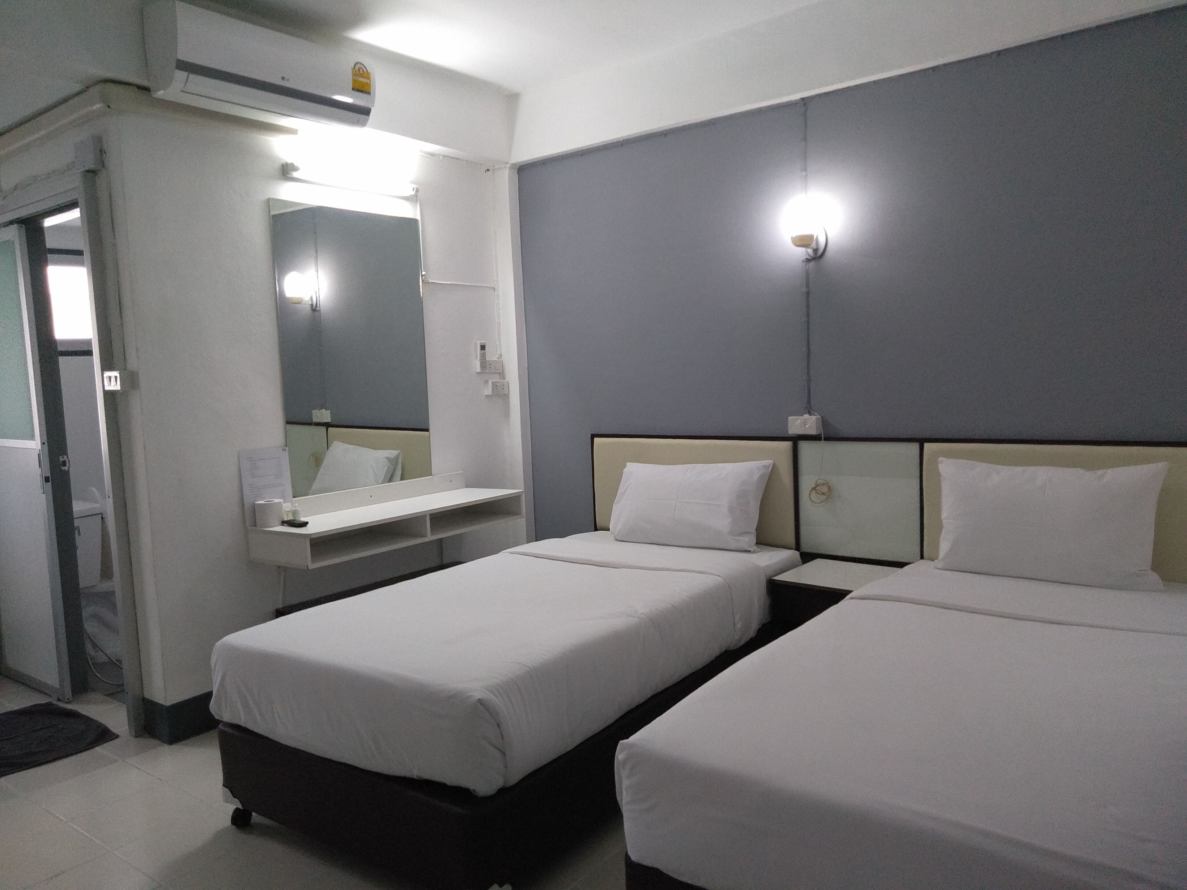 Habitación de hotel con dos camas, un escritorio pequeño, un espejo y una lámpara.