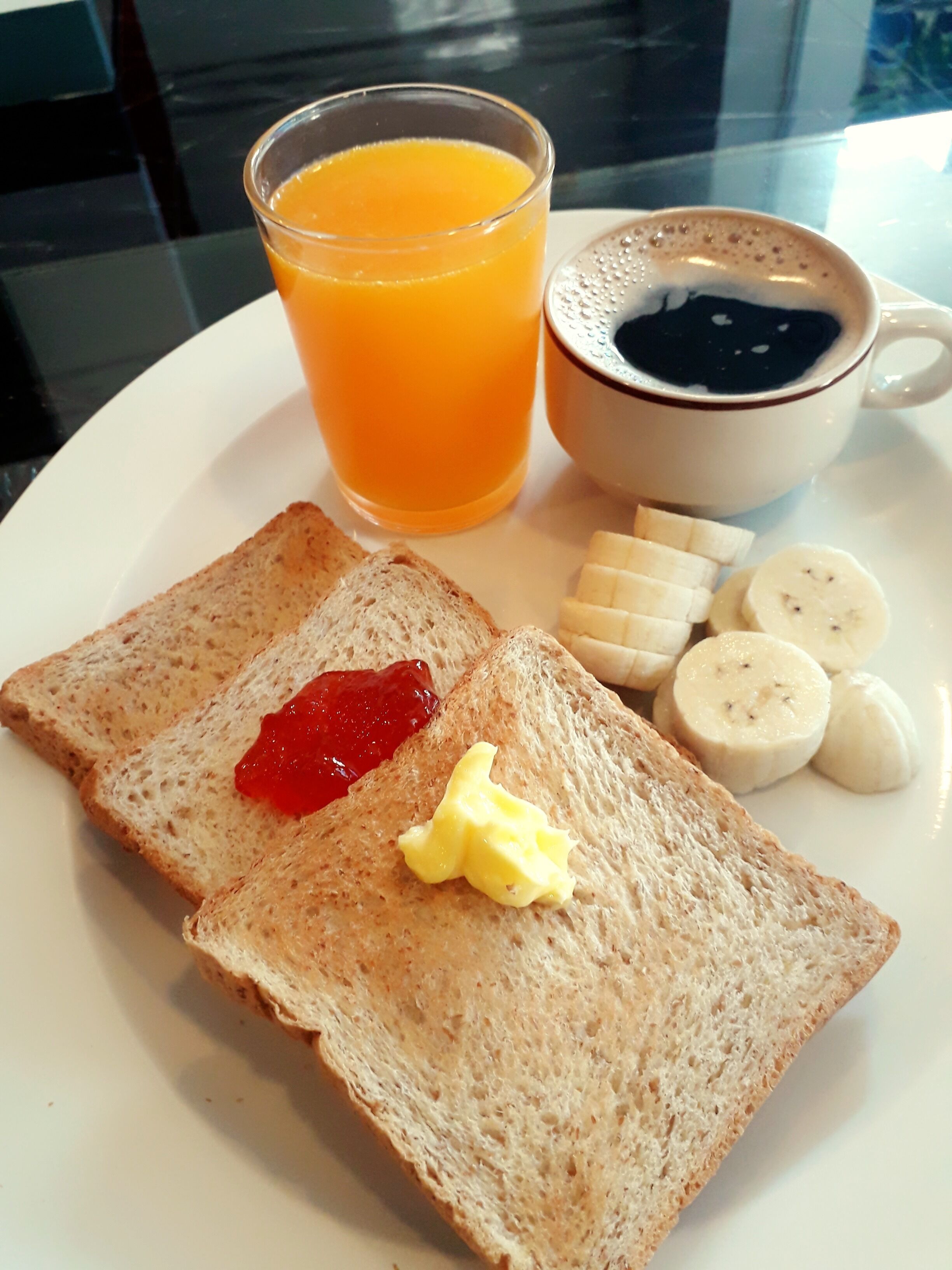A plate with toast, butter, jam, banana slices, a glass of orange juice, and a cup of coffee.