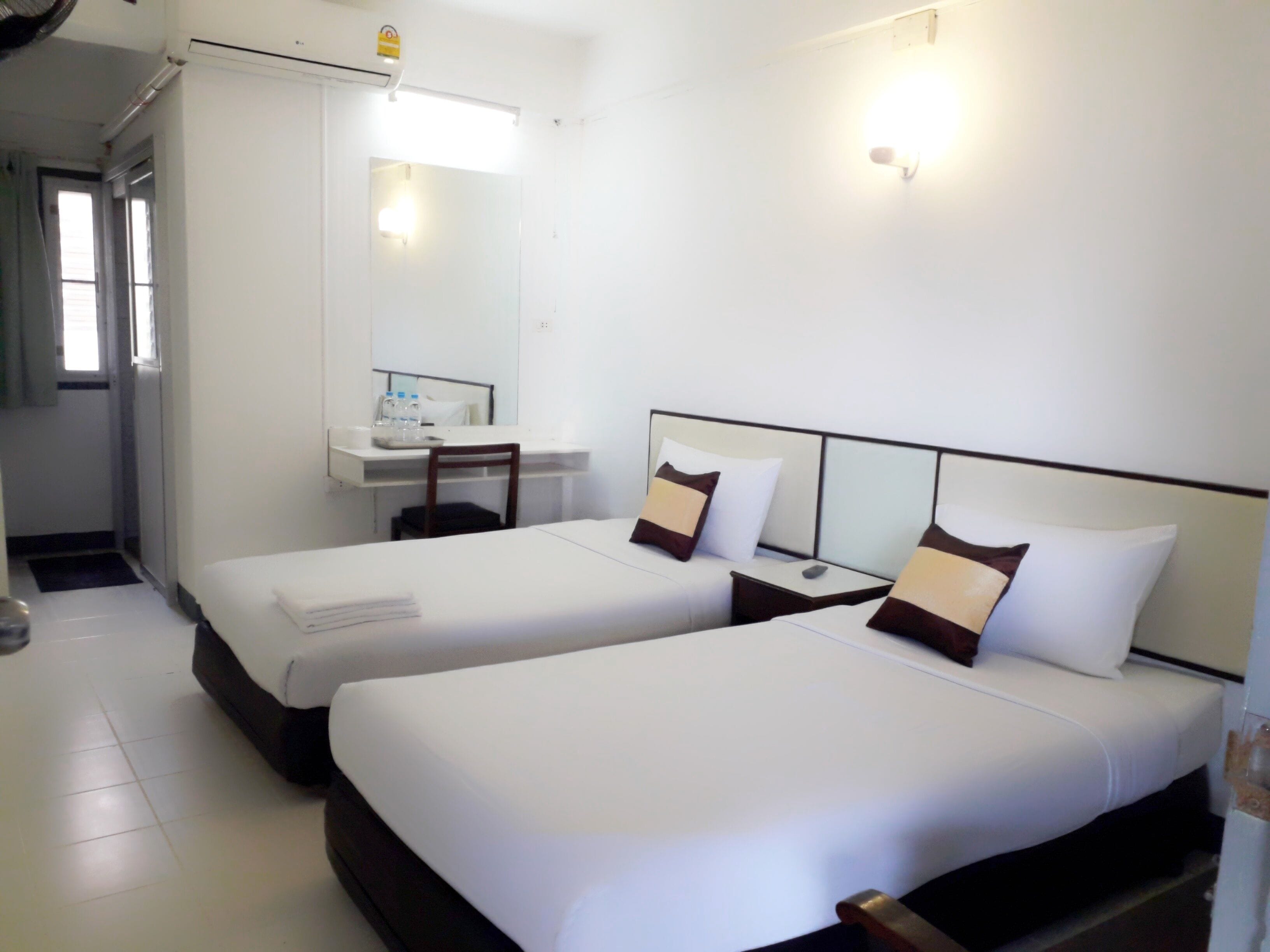 A hotel room with two beds, a desk, a chair, a mirror, and a bathroom door.