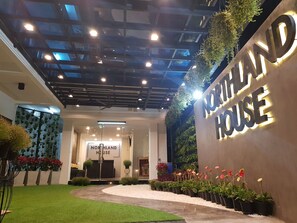 Entrada de um edifício moderno com uma placa indicando "NORTHLAND HOUSE" e uma área de jardim bem cuidada, com vasos de plantas e flores.