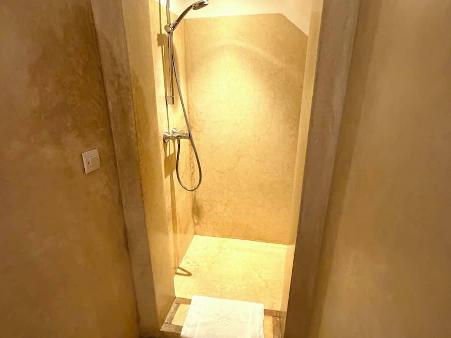 A small, enclosed shower area with a handheld showerhead, a towel, and a visible electrical outlet.