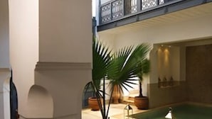 A spacious indoor courtyard with a pool, potted plants, and wicker furniture. - Riad Adore (Marrakech)