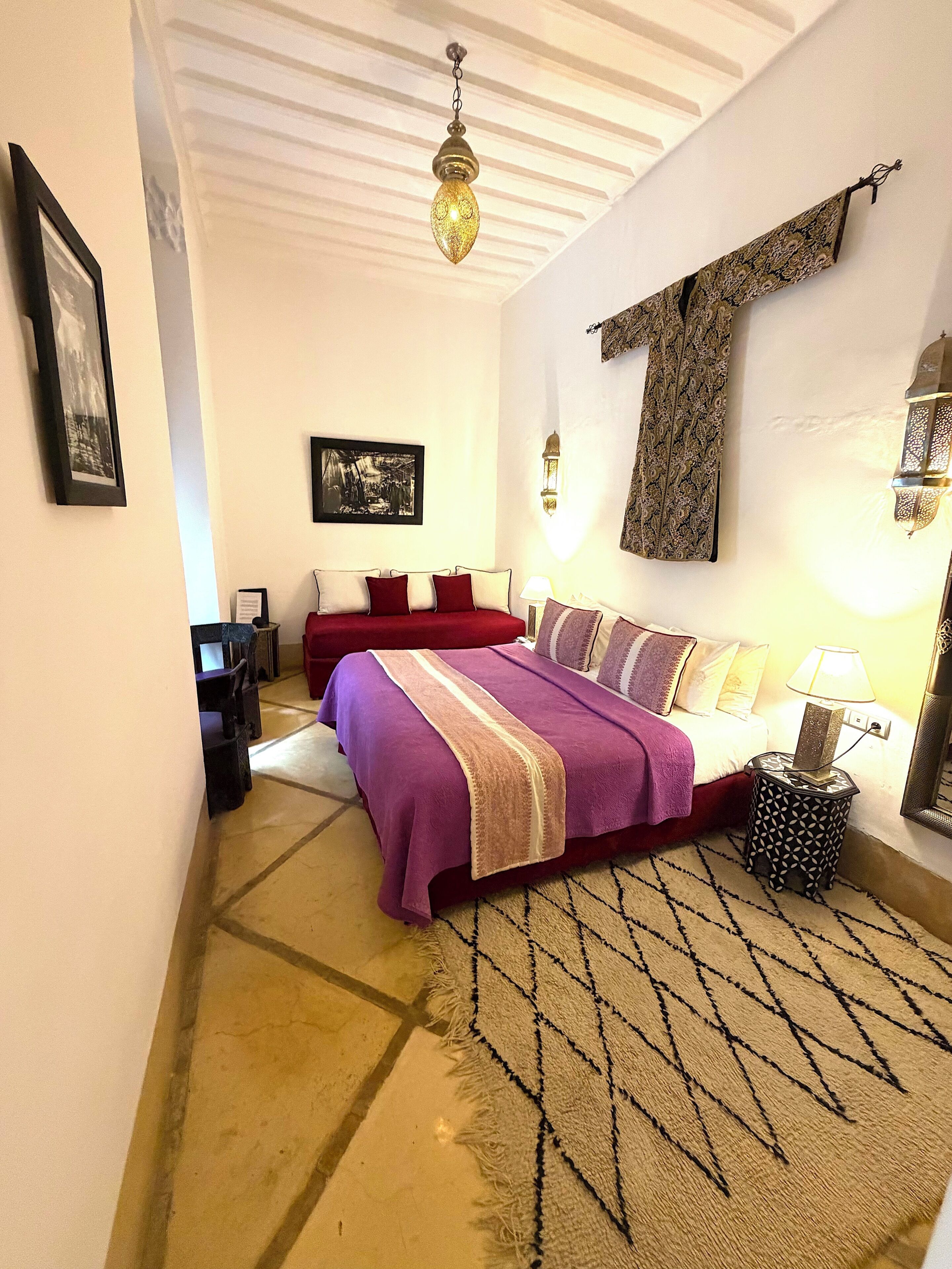 A bedroom with a bed, a nightstand, a wall-mounted lamp, and a ceiling light fixture.