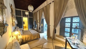 A bedroom with a bed, bedside lamps, a sofa, a table with a vase, and a view through a window. - Riad Adore (Marrakech)