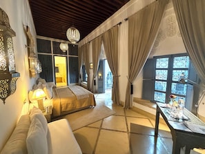 A bedroom with a bed, bedside lamps, a sofa, a table with a vase, and a view through a window. - Riad Adore (Marrakech)