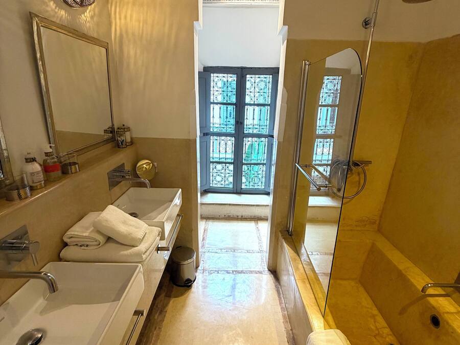 Een badkamer met twee wastafels, een douche, een grote spiegel en uitzicht op een binnenplaats door een raam.