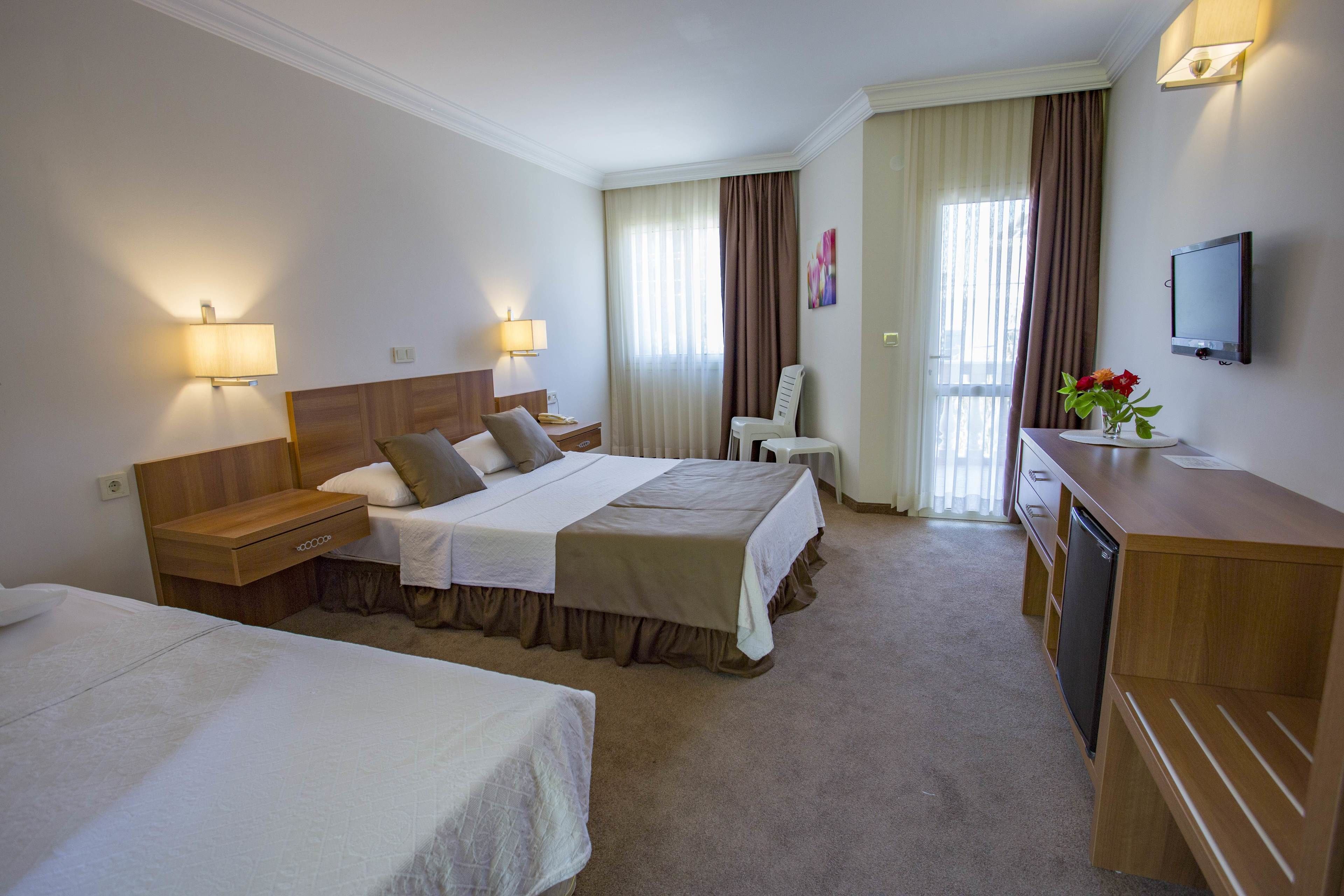 A hotel room with two beds, a desk, a chair, a TV, and a vase with flowers.